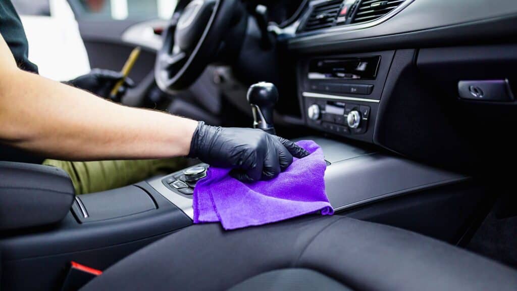 cánh tay đang dùng chiếc khăn màu tím để lau nội thất xe hơi